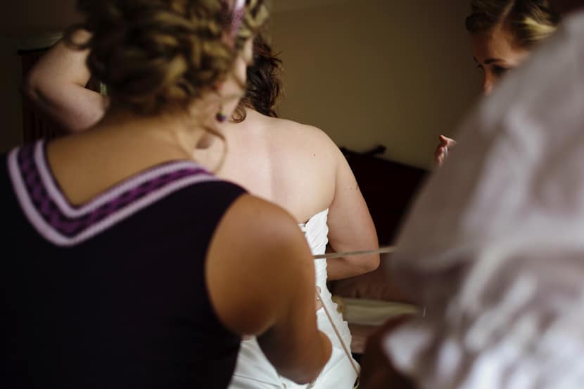 bridesmaids helping bride get dressed at Poet's Cove