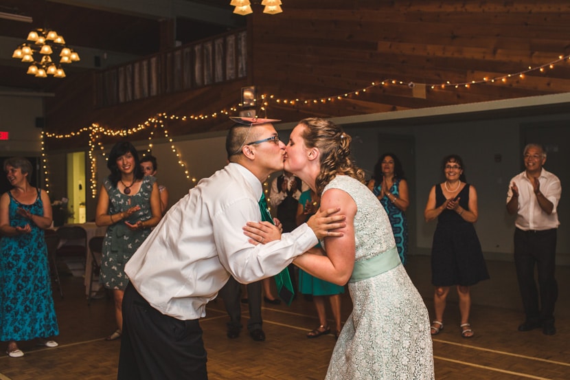 bride and groom kiss while guests watch at reception